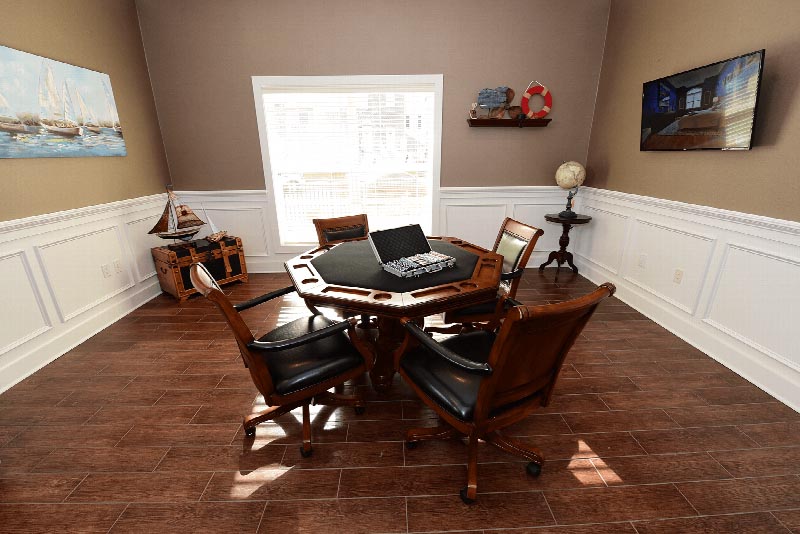 Image of the card room inside the Harbortown Clubhouse. There is a card table with seating for four. Playing cards and chips are displayed on the table. There is a window to allow for natural light, and several decorations around the room.
