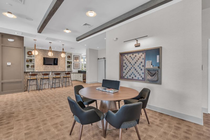 Interior image of the community room at the Rivendell Club House showing a seating area with a wall mounted scrabble board, and counter seating at the kitchen area.