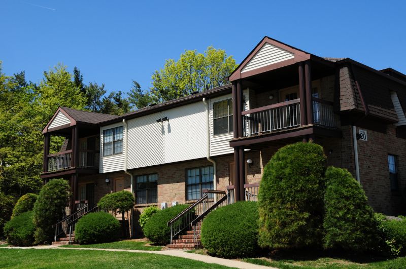 Woodbridge Center Plaza exterior imaging showing two townhomes with private entry and balconies. Green bushes and grass landscape the area. Larger trees can be seen behind the building.