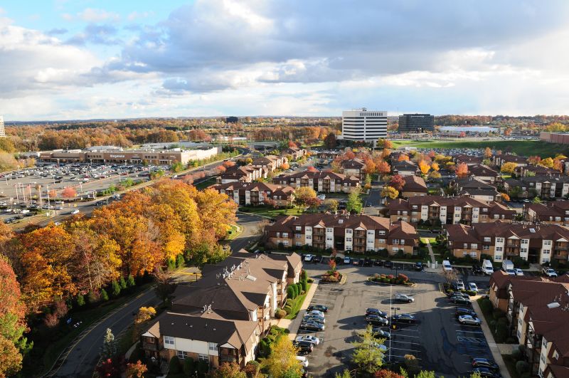 Woodbridge Center Plaza exterior image of the community showing parts of several buildings set among many trees and the Wegmans shopping center next door.