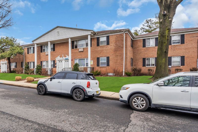 Cloverleaf Gardens exterior photo showing a brick exterior, a large tree in bloom with pink flowers, various bushes and green grass.