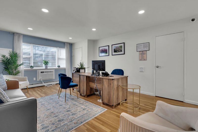Cloverleaf Gardens photo shows the living area in a refurbished apartment with hardwood floors and recessed lighting. The room is painted white with a blue accent wall. A coach, lamp and desk are shown.