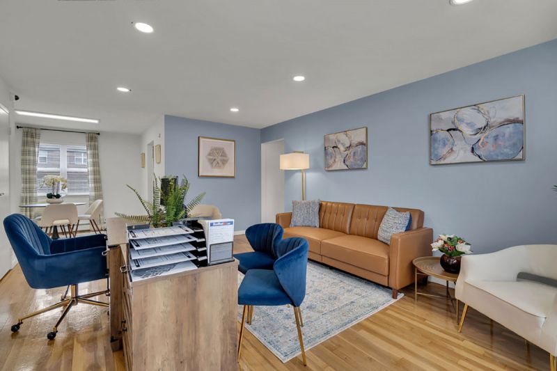 Cloverleaf Gardens photo shows the living area in a refurbished apartment with hardwood floors and recessed lighting. The room is painted white with a blue accent wall. A coach, lamp and desk are shown.