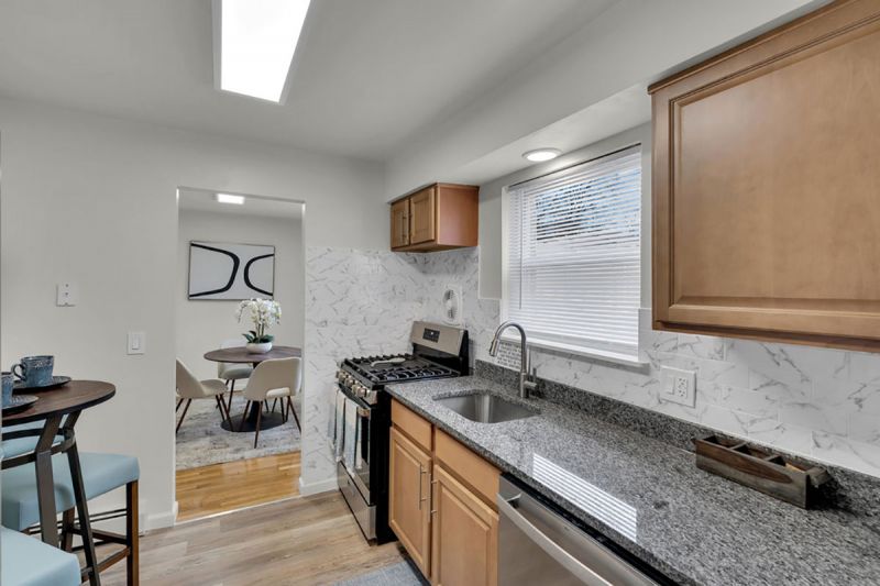 Cloverleaf Gardens photo shows the kithcen in a refurbished apartment with luxury vinyl tile flooring, new cabinets, granite countertops ad stainless steel appliances. The dining area can be seen in the background
