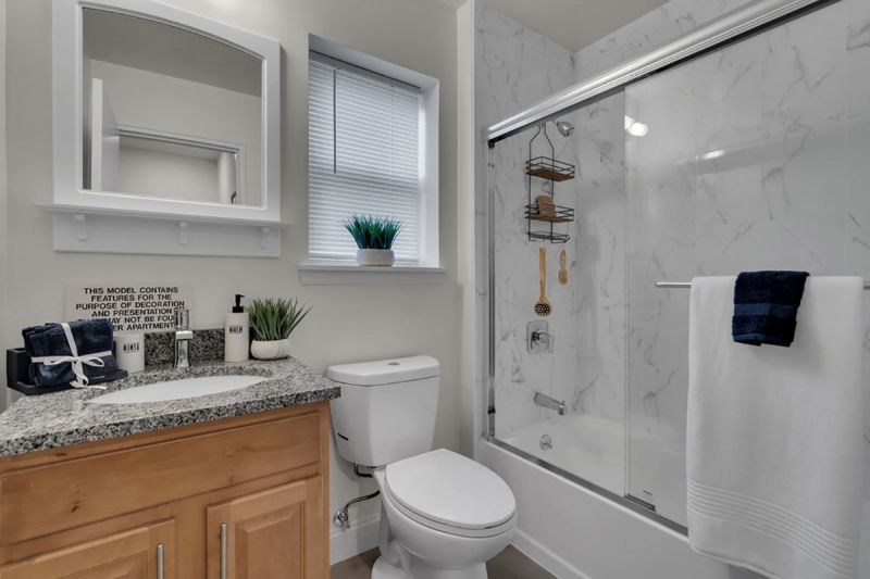 Cloverleaf Gardens photo shows the bathroom in a refurbished apartment with new shower doors and tile, new toilet and vanity with a new medicine cabinet. There is a window to allow for natural light.