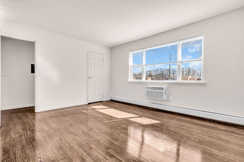 Interior photo of the bedroom at Cloverleaf Gardens luxury hardwood flooring and a large window that fills the space with natural light. On the left, a door provides access to the hallway, while another door opens to a spacious closet.