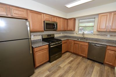 Photo of a renovated kitchen at Forest View showing vinyl wood plank flooring, granite countertops, new appliances, new cabinets and mosaic tile backsplash.