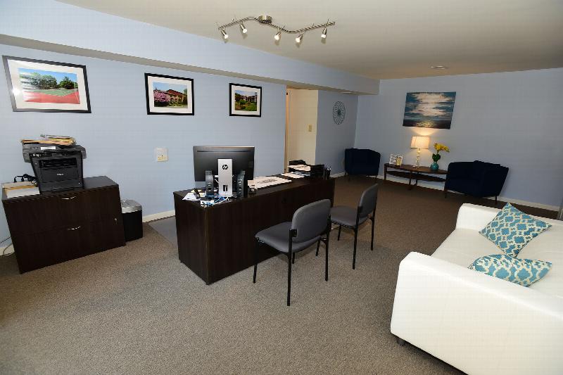 Gill Lane photo of the rental office area set up in the living room of the model. A couch offers seating for guests, a desk with several chairs for discussing options with customers is shown.