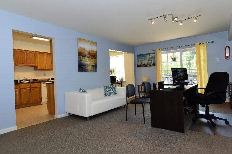Gill Lane photo of the rental office area set up in the living room of the model. A couch offers seating for guests, a desk with several chairs for discussing options with customers is shown.