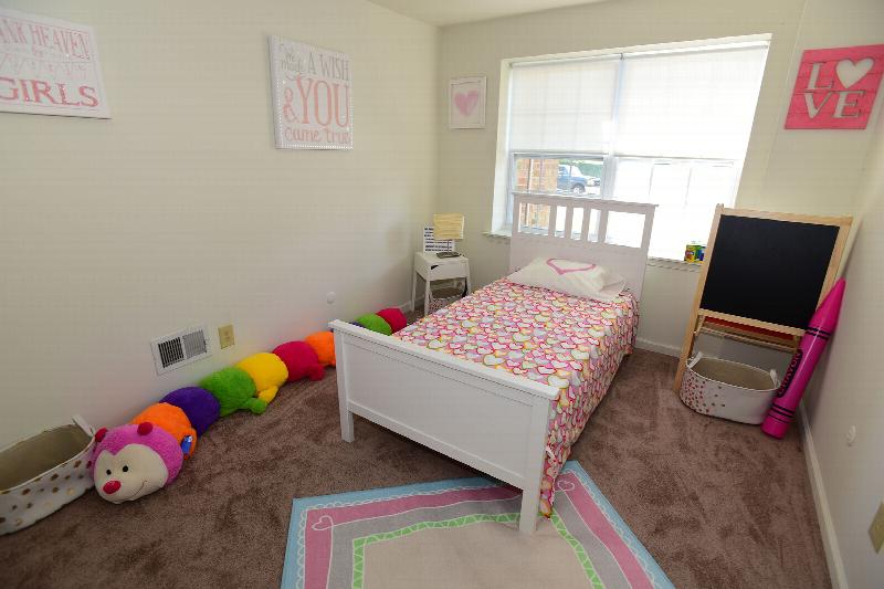 Gill Lane kids bedroom photo shows a bed and various kids toys. A double window lets in natural light.
