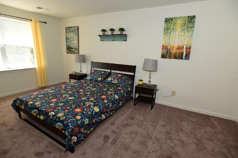 Gill Lane bedroom photo shows a bed with two night stands with lamps. Several pieces of artwork are displayed on the walls. A large double window lets in natural light.