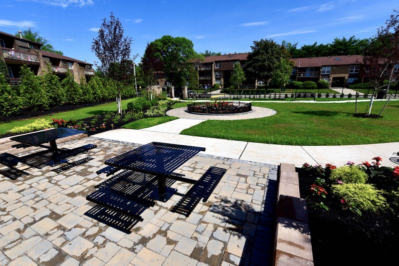 Photo of park area at Gill Lane showing a paver patio with tables and benches, several flower gardens and some open green space