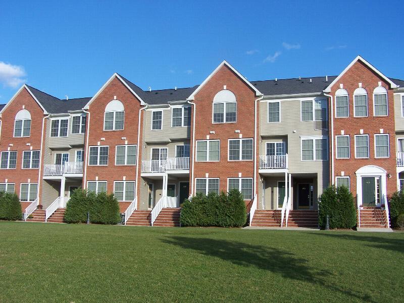 Sun Valley photo of a 3 story apartment building with red brick and white vinyl siding. There are several staircases leading to private entry front doors. There is a large green lawn in front of the building and various bushes landscape the area.