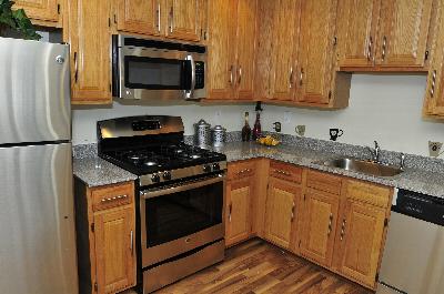 Sun Valley Affordable apartment’s kitchen photo showing maple colored cabinets, wood grain flooring, granite countertops and stainless steel appliances.