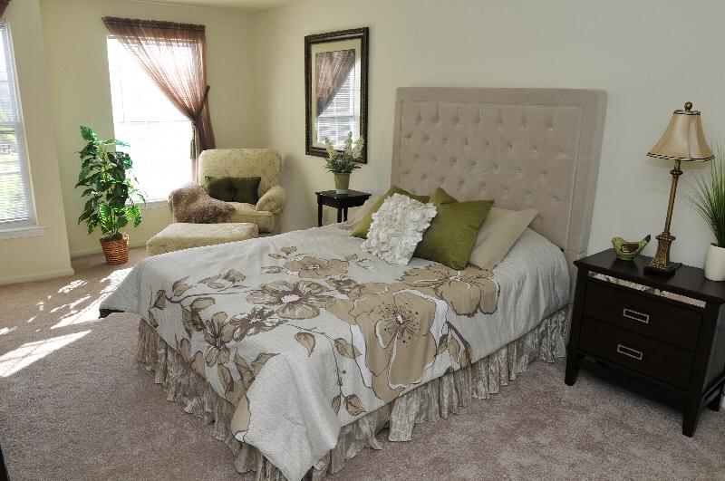 Sun Valley Affordable photo of a master bedroom showing a bed with two end tables, a chair with ottoman, and several windows allowing in natural light. There is lush wall-to-wall carpeting and several large windows letting in natural light.