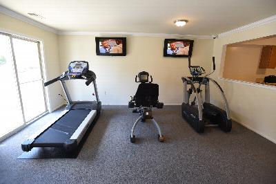 Rivendell Heights Affordable Exercise Room showing a treadmill, an exercise bike and an elliptical. There are two T.V.'s on the wall and large windows to allow natural light to enter the room.