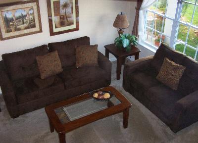 Tall Oaks at Monroe Manor Affordable living room photo shows a seating area with a coffee table and an end table. There are several pieces of wall art on display, as well as a table lamp and plant on the end table.