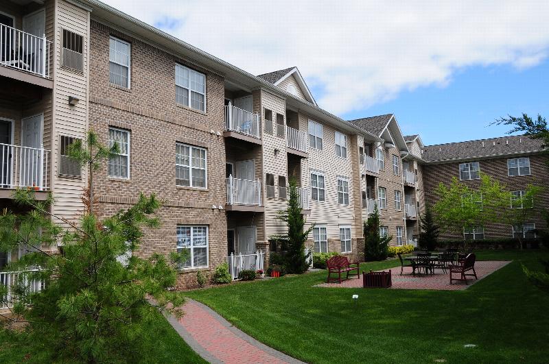 Exterior photo of the courtyard at Park Terrace featuring several seating areas on a large patio. Green grass, shrubs and trees landscape the area.