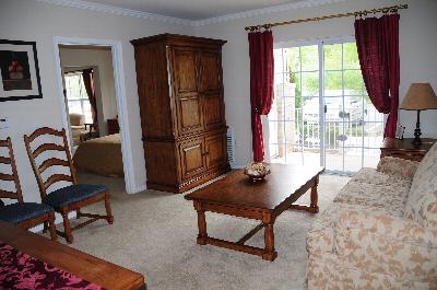 Photo of a living room inside a Park Terrace apartment. There is a couch and several chairs, an end table with a lamp and a coffee table. Sliding glass doors lead to a balcony.