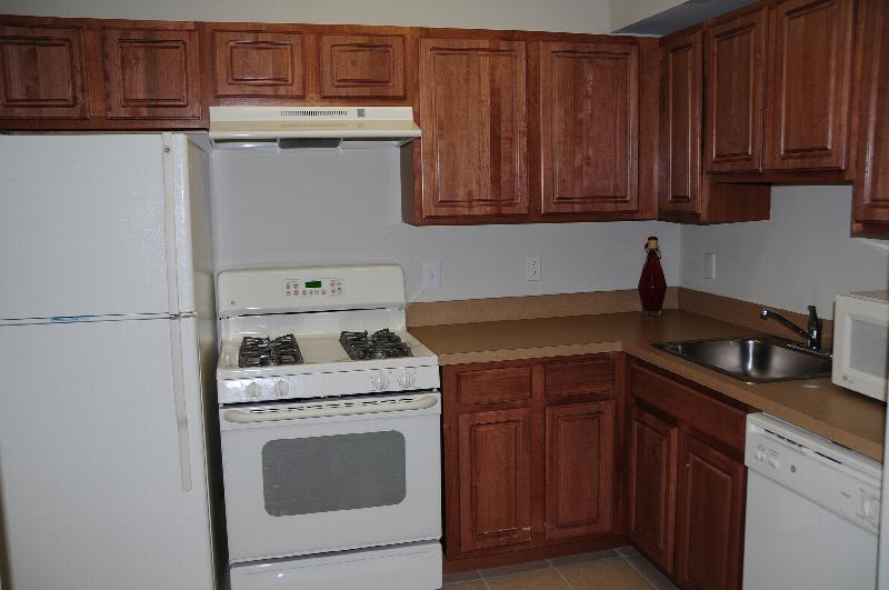 Park Terrace photo of a kitchen showing warm cherry colored cabinets, a countertop and white appliances.