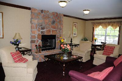 Photo of the community room at Park Terrace showing a large seating area around a fireplace with a large coffee table. There is also a table with chairs in front of a window which allows for natural light.