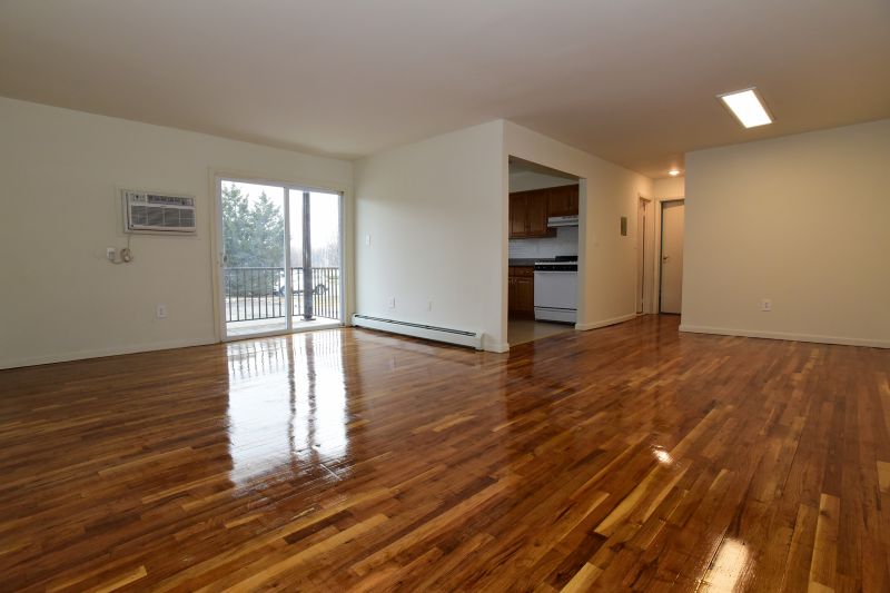 Woodbridge Village living room photo shows shiny hardwood floors leading to sliding glass doors to a balcony, the kitchen entry can also be seen.