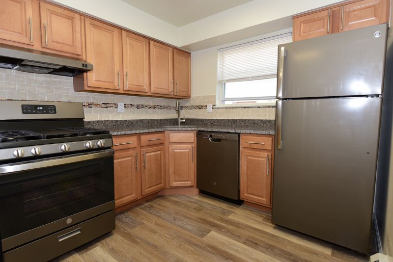 Photo of renovated kitchen showing wood grain tile flooring, new cabinets with granite counter tops and a stainless steel appliance package.