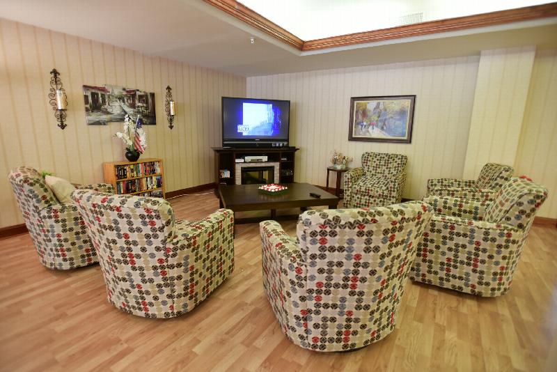 Yorkshire Village community room showing six chairs, a large table, an entertainment center with a TV and a shelf with a VHS collection. Several decorations are located on the tables and on the wall.