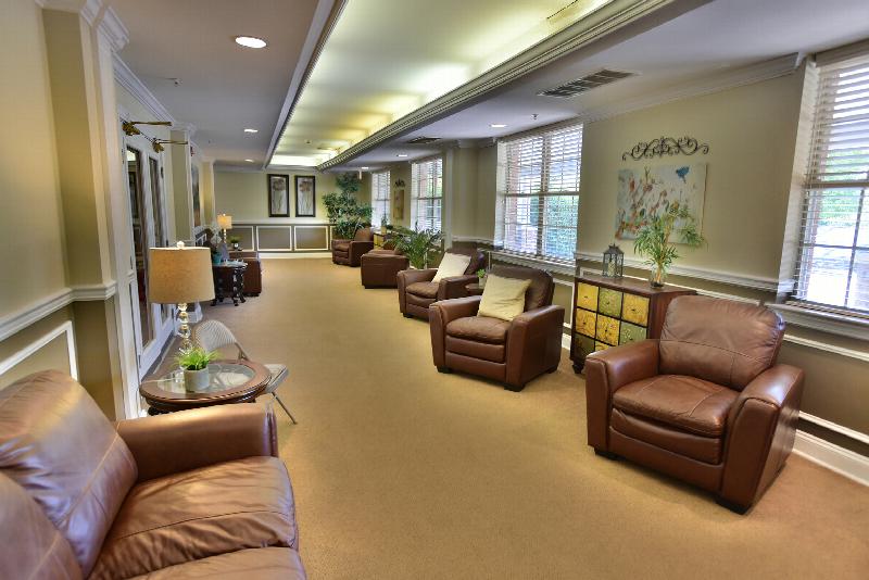 Yorkshire Village common area showing seven leather chairs and several end tables. There are three windows to allow natural light to enter the room. There are several decorations on the tables and on the walls.