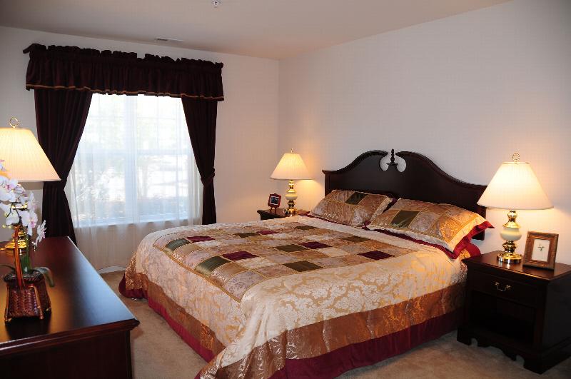 Hyde Park Bedroom photo showing a queen sized bed, a dresser and two nightstands with lamps. There are several decorations on the dresser and nightstands. There is a large window with curtains that allows natural light to enter the room.