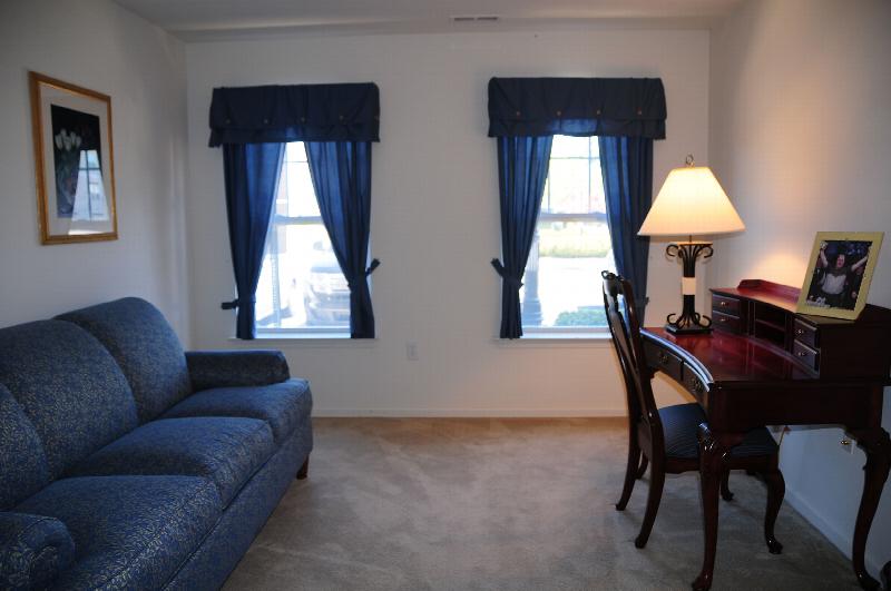 Hyde Park Interior photo showing a couch, a desk and a chair. There is a lamp and a picture on the desk. There are two windows with curtains to allow natural light to enter the room.