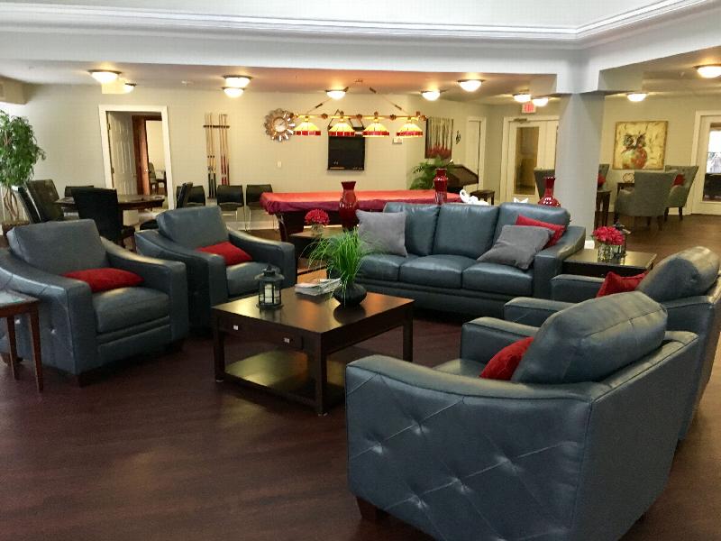 Hyde Park Community Room showing a couch and several chairs surrounding a table with decorations. There is a pool table with chairs and pool cues. There are two tables with four seats around each table. There are pictures on the wall and decorations throughout the room.