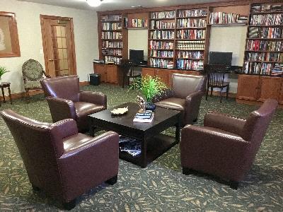 Hyde Park Community Room photo showing four leather chairs and a table with decorations. There are two computers with chairs on the counter against the wall. On the counters are several book shelves filled with books. There is an end table with a chair against the wall.