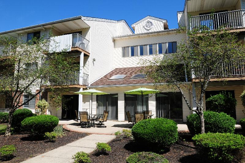 Edison Woods Seniors for ages 55 and over shows an outdoor community seating area with tables and umbrellas surrounded by landscaping.