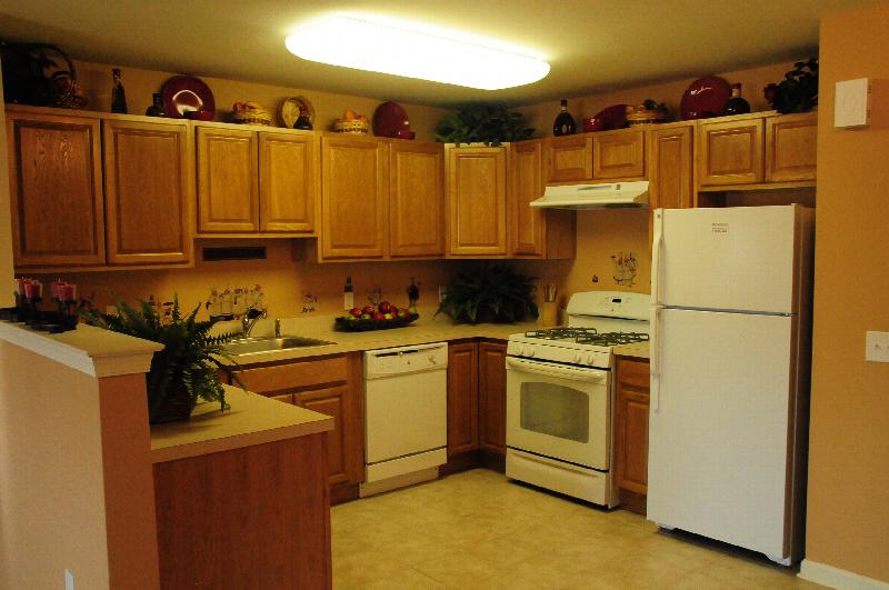 Village at Stratford for ages 55 and above image of the kitchen shows plenty of cabinets, a counter top and white appliances. Many decorations are shown above the cabinets and on the countertop.