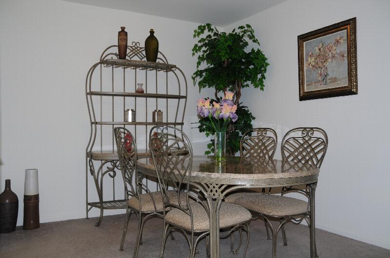 Pike Run Affordable Dining Room photo with carpet flooring. There is a 4 person table with chairs with a shelf and decorations against the wall. There are flowers on the table and a plant in the corner of the room.