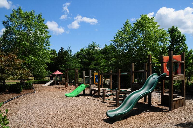 Pike Run Affordable exterior photo showing the playground. Several bushes and trees highlight the landscape.