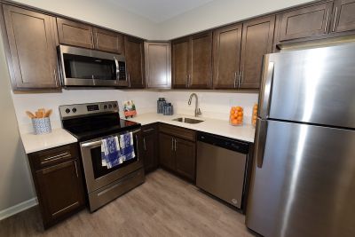 Photo of a refurbished kitchen at Edison Village showing LVT woodgrain flooring, new cabinets and countertop with stainless steel appliances.
