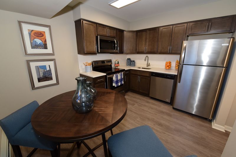 Photo of a refurbished kitchen at Edison Village showing LVT woodgrain flooring, new cabinets and countertop with stainless steel appliances with small dining table