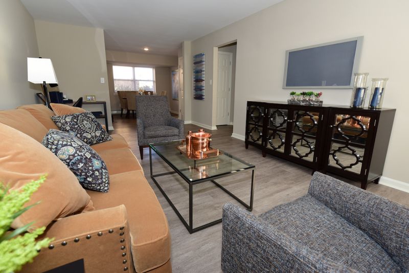 Photo of a living room in a refurbished apartment at Edison Village showing LVT woodgrain flooring, couch, coffee table, large screen TV above a credenza.