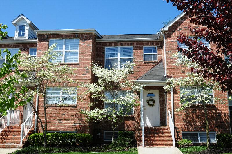 Homestead Village exterior photo of a full brick apartment building showing multiple staircases leading to front doors. Green grass, shrubs and flowering trees landscape the front of the building.