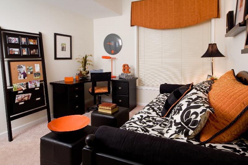 Helix at Xchange Affordable interior photo of second bedroom shows a day bed with decorative pillows and two ottomans located in front it. An office table, chair and decorative wall display can be seen in the back ground. 