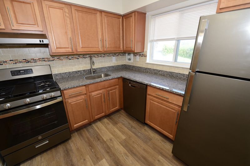 Photo of renovated kitchen showing wood grain tile flooring, new cabinets with granite counter tops and a stainless steel appliance package.