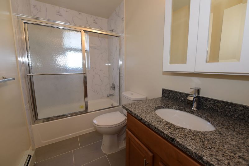 Photo showing a freshly painted renovated bathroom showing new ceramic tile flooring, new tub with shower doors, new toilet, sink, vanity and medicine cabinet.