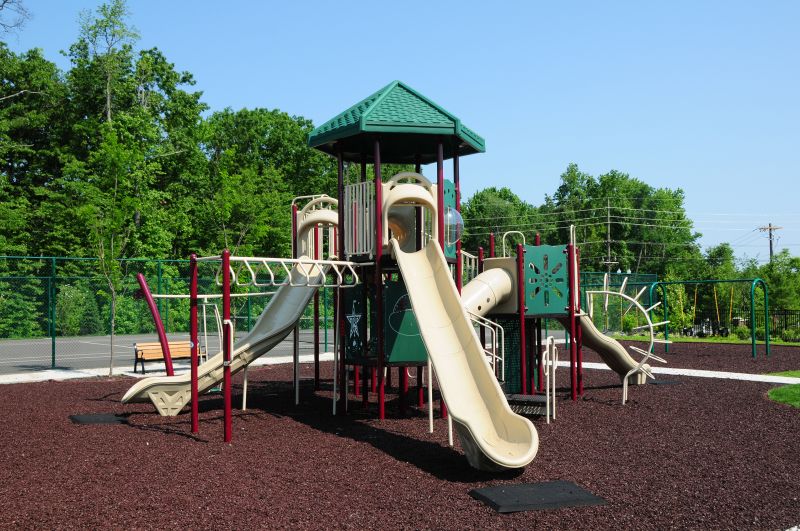 Princeton Terrace at West Windsor Affordable playground photo with a swing set. A tennis court surrounded by a fence. Several trees highlight the landscape.