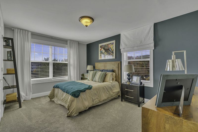 Interior Photo of the model at Princeton Terrace at West Windsor showing a bedroom with bed, night stand and dresser with wall to wall carpeting. Large double window to allow for natural light. 