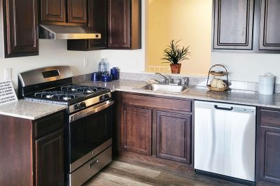 Evergreen East apartments interior photo of the living room shows a kitchen showing cherry cabinets, granite countertops, woodgrain tile flooring, and stainless steel appliances.