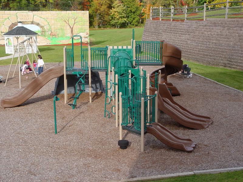 Sun Valley community playground area showing a large piece of children’s play equipment with multiple slides, a swing set, and benches.
