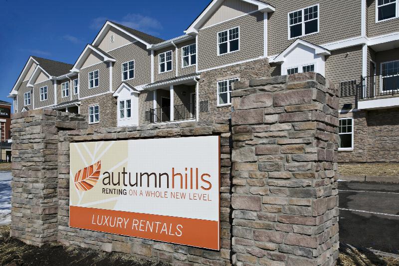 Autumn Hills exterior photo featuring the entrance sign. The logo for Autumn hills is featured, along with the tagline of Renting On A Whole New Level. The term Luxury Rentals is also featured on the sign. One of the apartment buildings is shown in the background.