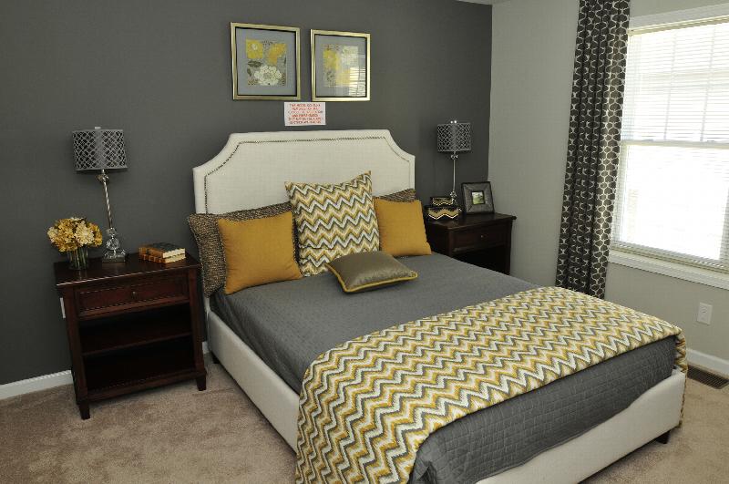 Autumn Hills bedroom photo shows a queen sized bed and two night stands with lamps. Window treatments, wall art and other items decorate the room.